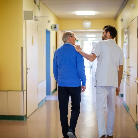 Personnel soignant accompagne un patient dans un couloir.
