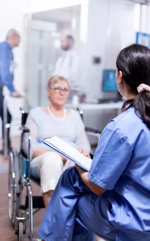 Une femme en fauteuil roulant accompagnée d'une infirmière la rassurant.