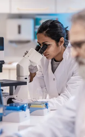 Deux médecins dans un laboratoire médical dont une médecin regardant dans un microscope. Groupe Vivalto Santé