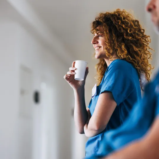 Infirmière avec un café à la main, regardant un patient en souriant.