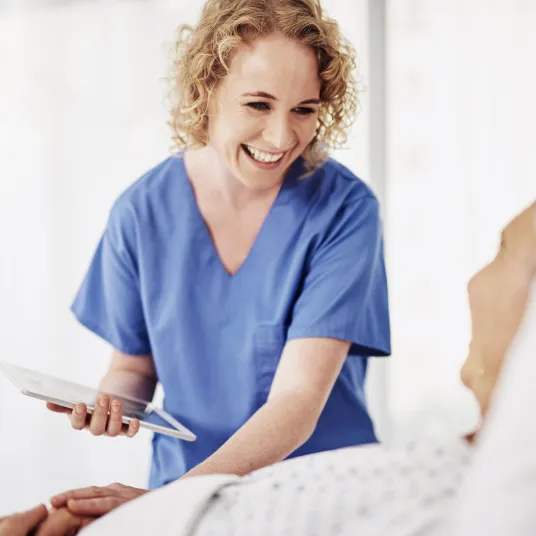 Infirmière souriant à un patient alité, Groupe Vivalto Sante