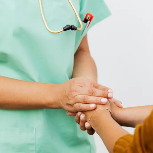 Une infirmière en vert tenant la main d'un patient de manière bienveillante