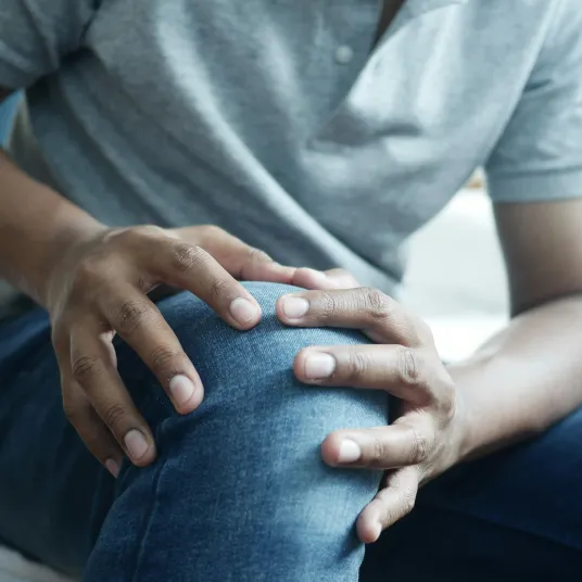 Zoom sur une personne touchant son genou avec ses deux mains à cause de la douleur - Groupe Vivalto Santé