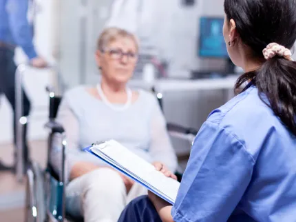 Une femme en fauteuil roulant accompagnée d'une infirmière la rassurant.