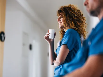 Infirmière avec un café à la main, regardant un patient en souriant.
