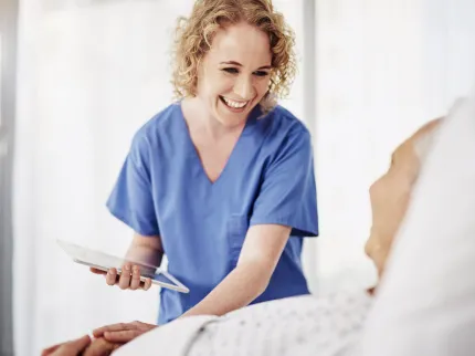 Infirmière souriant à un patient alité, Groupe Vivalto Sante