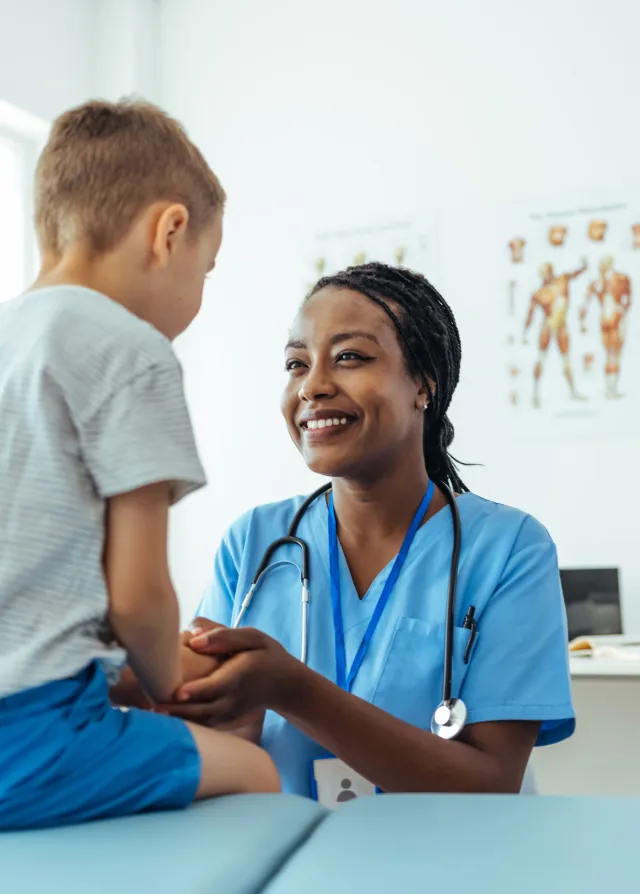>Un petit garçon sur une table de consultation avec un infirmière lui souriant de manière rassurante, Groupe Vivalto Santé