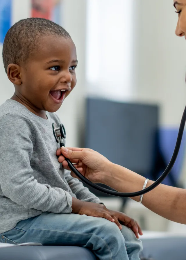 Un petit garçon sur une table de consultation en train de se faire ausculter par une infirmière écoutant son cœur grâce à un stéthoscope, Groupe Vivalto Santé
