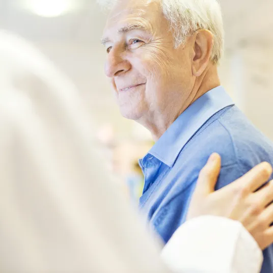Patient agé souriant au médecin qui lui touche l'épaule en signe d'empathie, Groupe Vivalto Santé