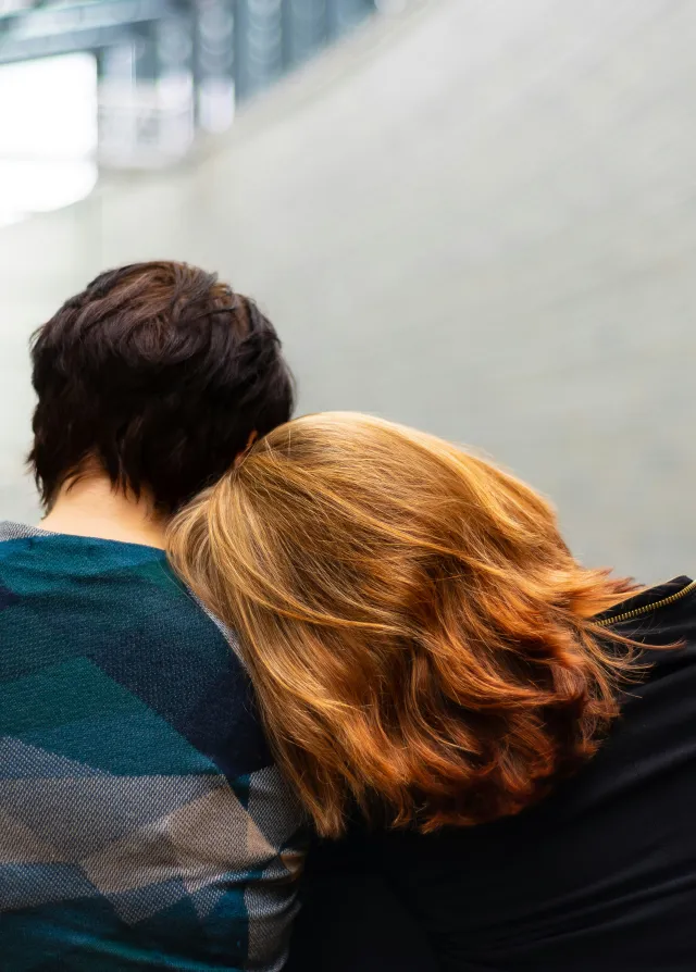 Un couple assis l'un à côté de l'autre dans le hall d'un hôpital. La femme aux cheveux roux pose sa tête sur l'épaule de son compagnon.