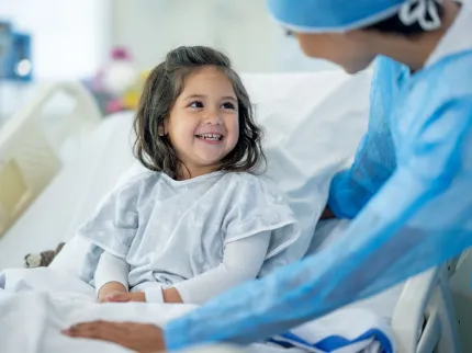 Petite fille dans son lit d'hôpital, souriant à l'infirmière qui s'occupe d'elle.
