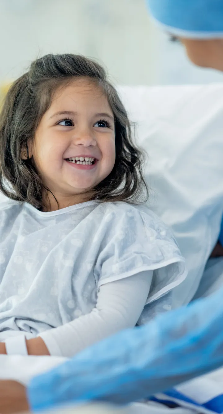 Petite fille dans son lit d'hôpital, souriant à l'infirmière qui s'occupe d'elle.