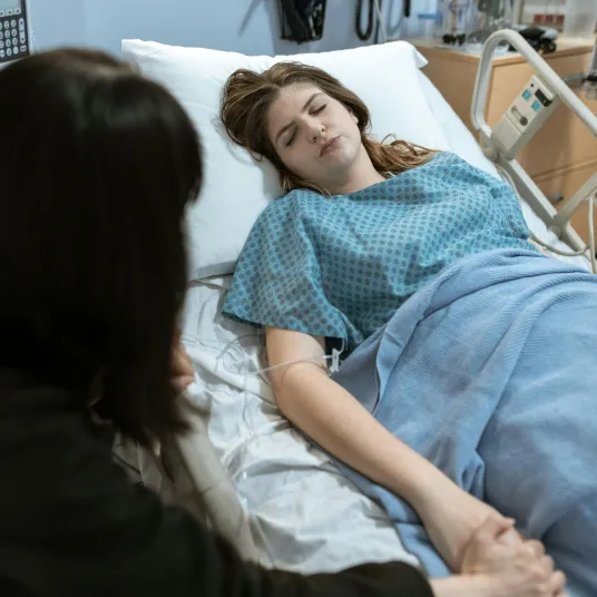 Une femme venue rendre visite à son amie à l'hôpital. Elle lui tient la main alors que la patiente dors. 