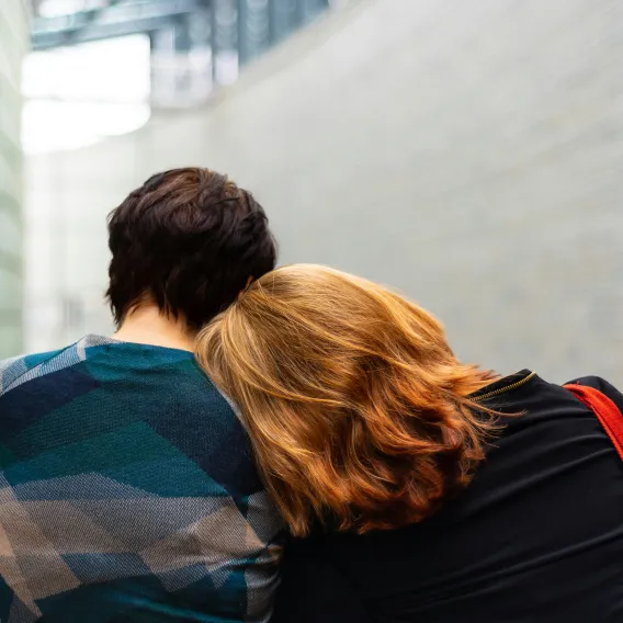 Un couple assis l'un à côté de l'autre dans le hall d'un hôpital. La femme aux cheveux roux pose sa tête sur l'épaule de son compagnon.