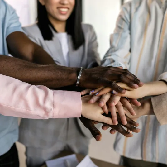 Groupe de personne regroupant leur main ensemble en signe de cohésion et de travail d'équipe.