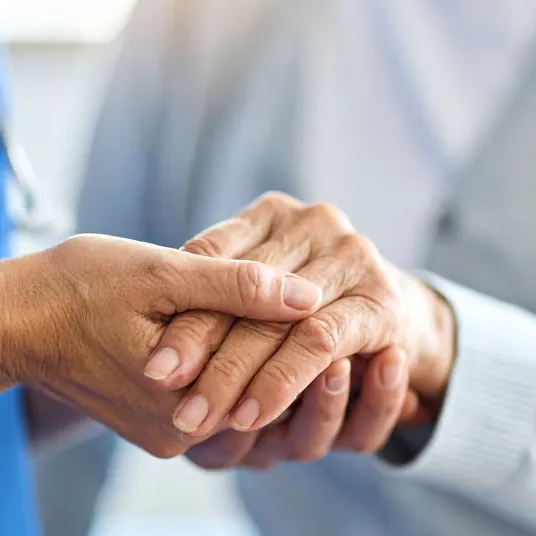 Une soignante tient la main d'une personne âgée