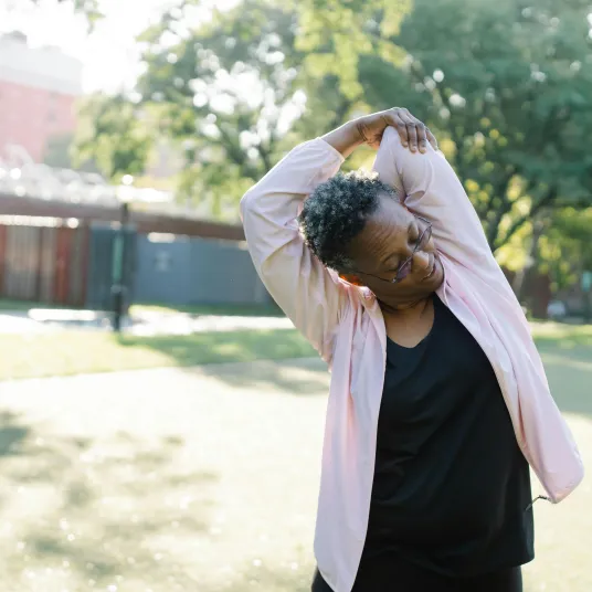 Femme âgée s'étirant le dos en se touchant le coude - Groupe Vivalto Santé