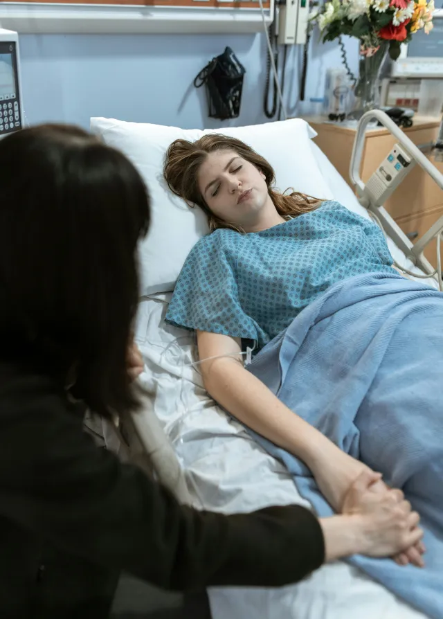 Une femme venue rendre visite à son amie à l'hôpital. Elle lui tient la main alors que la patiente dors. 