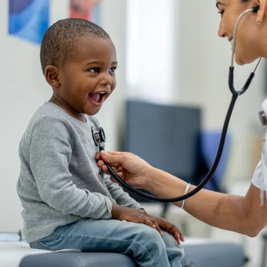 Un petit garçon sur une table de consultation en train de se faire ausculter par une infirmière écoutant son cœur grâce à un stéthoscope, Groupe Vivalto Santé