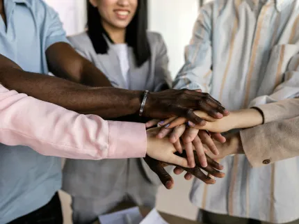 Groupe de personne regroupant leur main ensemble en signe de cohésion et de travail d'équipe.