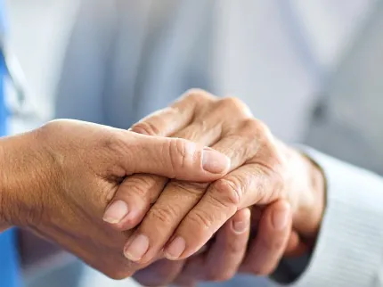 Une soignante tient la main d'une personne âgée