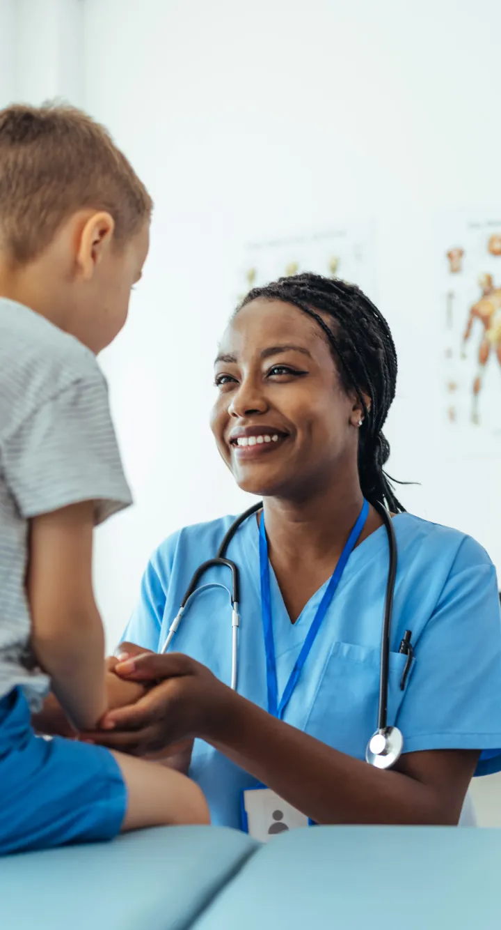 >Un petit garçon sur une table de consultation avec un infirmière lui souriant de manière rassurante, Groupe Vivalto Santé
