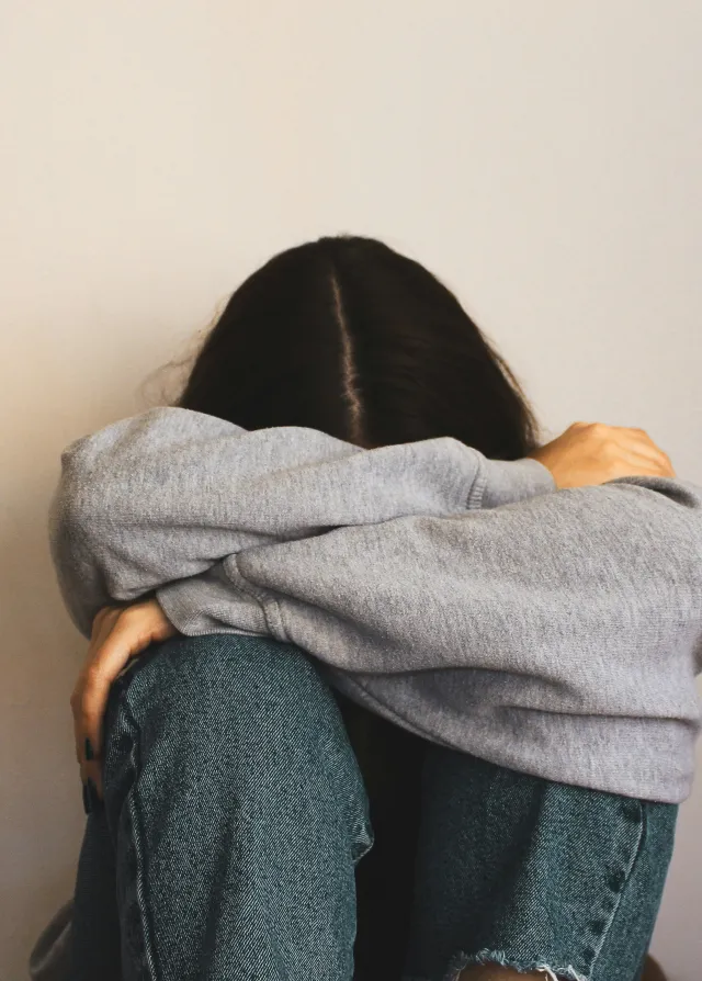 Zoom sur une femme adossée contre un mur, ses jambes sont repliées et elle pleure, la tête dans ses bras. 