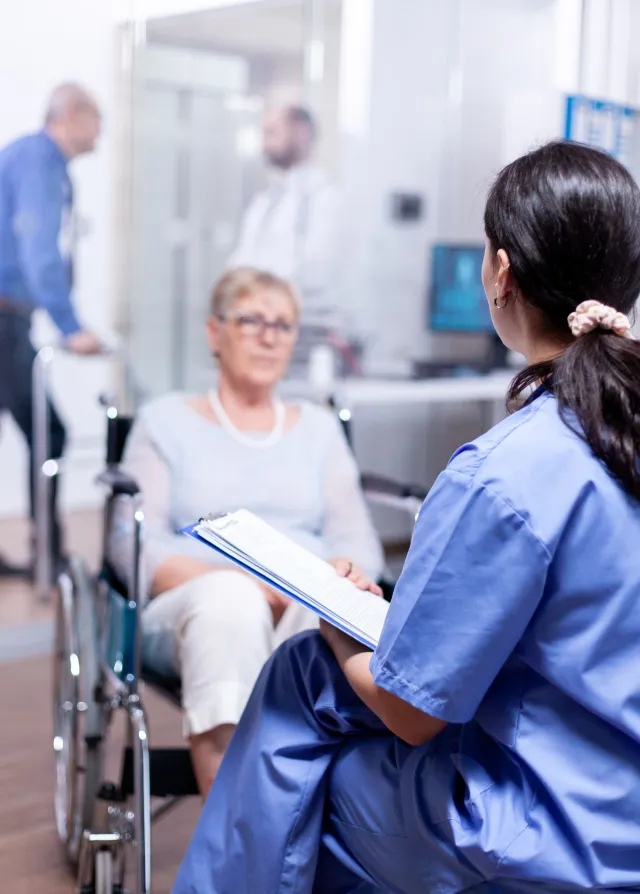 Une femme en fauteuil roulant accompagnée d'une infirmière la rassurant.