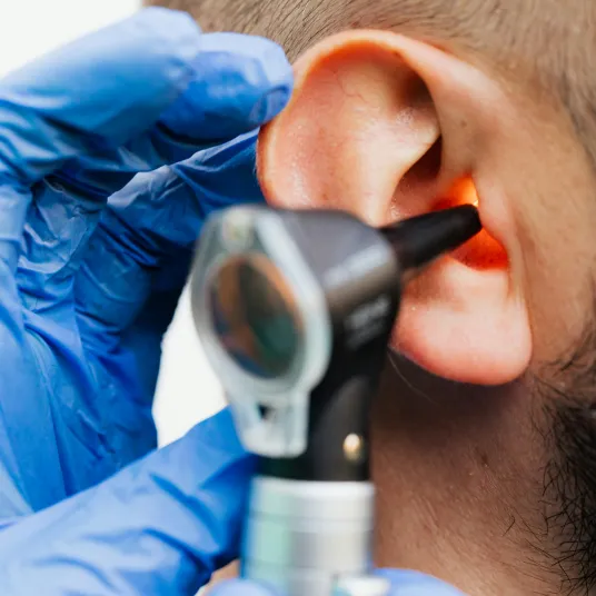 Praticien avec un otoscope dans l'oreille d'un patient en consultation ORL.