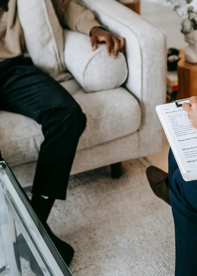 Un patient assis sur un canapé en face de son médecin. Il lui raconte le problème qu'il a et le médecin prend des notes. 
