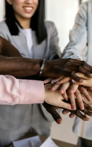 Groupe de personne regroupant leur main ensemble en signe de cohésion et de travail d'équipe.