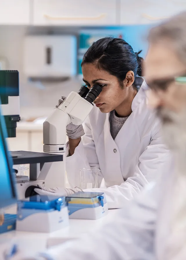 Deux médecins dans un laboratoire médical dont une médecin regardant dans un microscope. Groupe Vivalto Santé