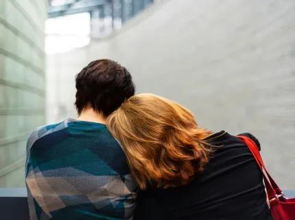 Un couple assis l'un à côté de l'autre dans le hall d'un hôpital. La femme aux cheveux roux pose sa tête sur l'épaule de son compagnon.