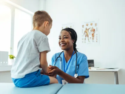 >Un petit garçon sur une table de consultation avec un infirmière lui souriant de manière rassurante, Groupe Vivalto Santé