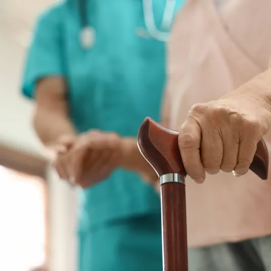 Zoom sur la canne d'une personne âgée, accompagnée d'une infirmière. 